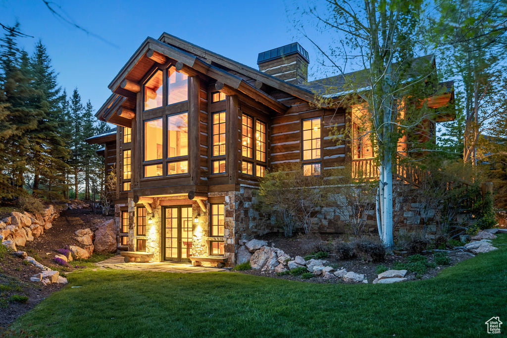 Rear view of property featuring a chimney, a lawn, and stone siding