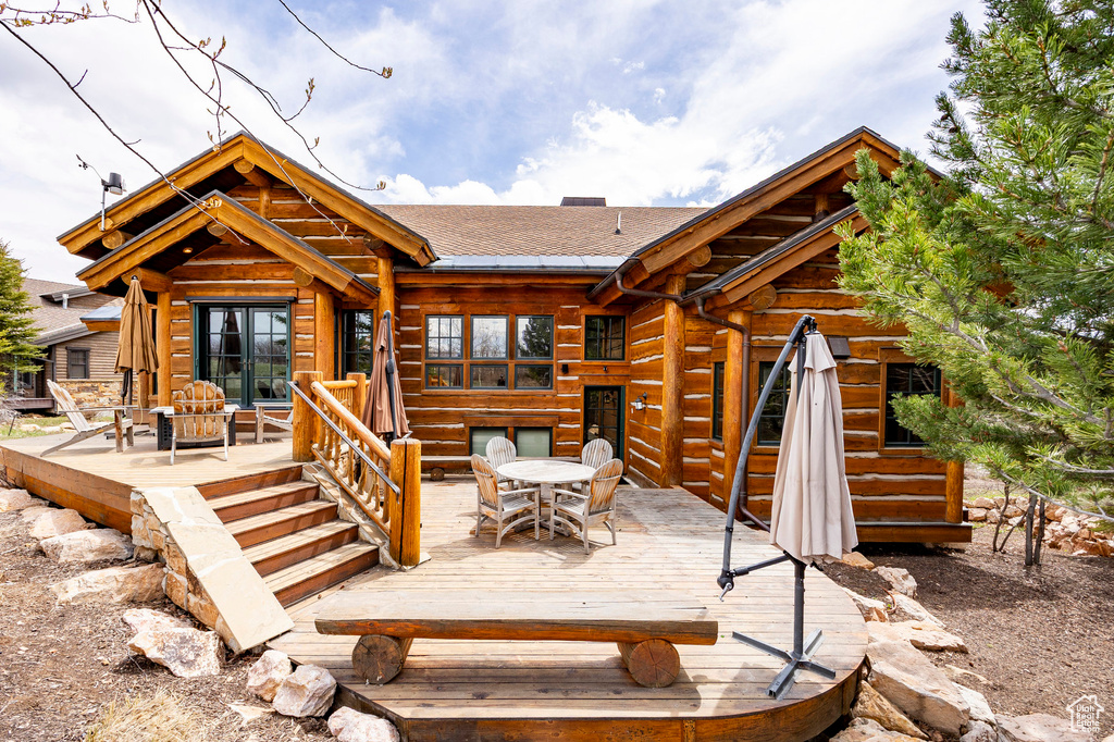 Rear view of house with outdoor dining area, a deck, and roof with shingles