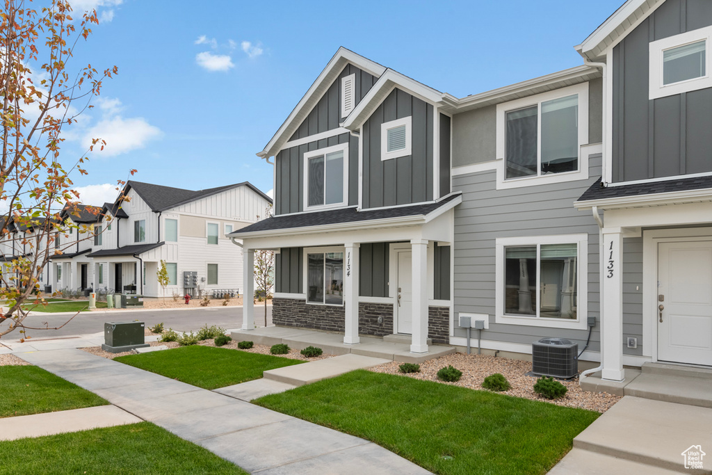 View of front of property with board and batten siding, covered porch, central AC unit, a front lawn, and a residential view