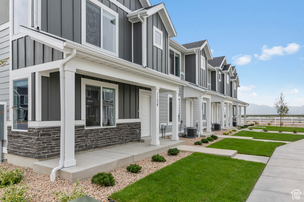 View of property exterior with board and batten siding, a porch, central AC, and stone siding
