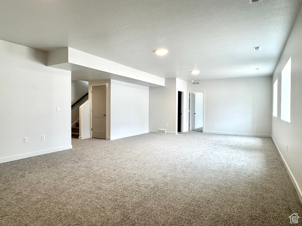 Basement featuring stairway, carpet, baseboards, and a textured ceiling