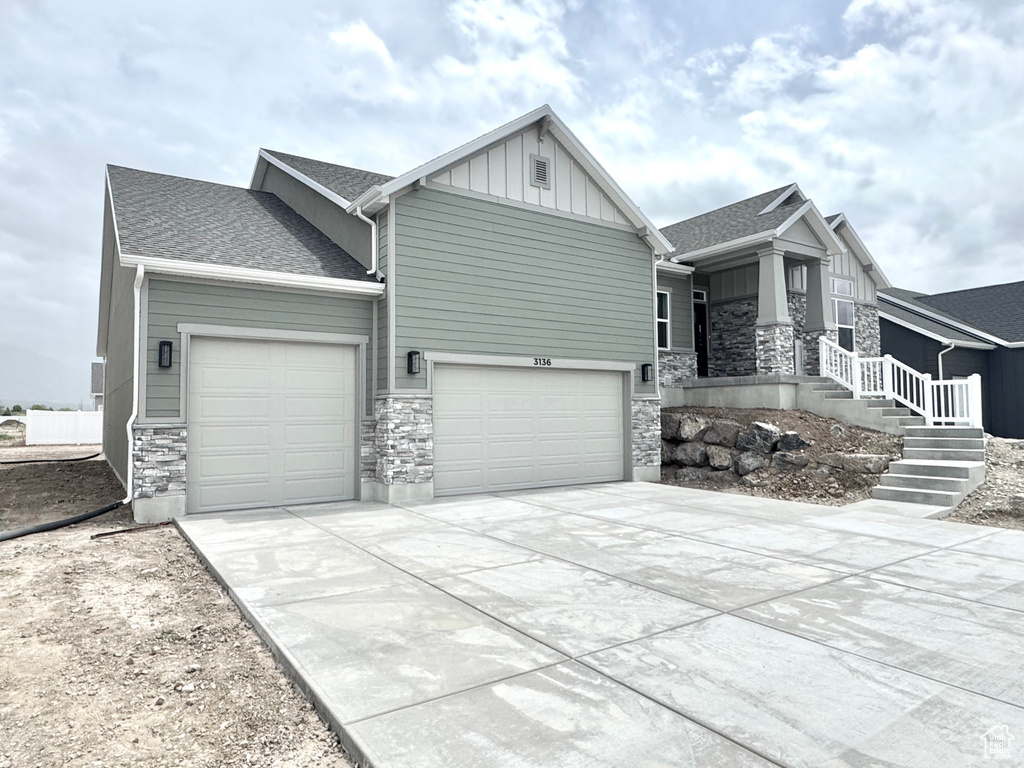 View of front of property with stone siding, an attached garage, board and batten siding, and concrete driveway