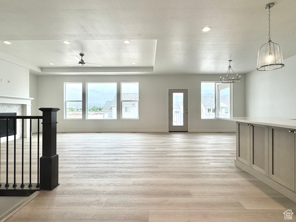 Unfurnished living room with light wood finished floors, a ceiling fan, recessed lighting, a chandelier, and a raised ceiling
