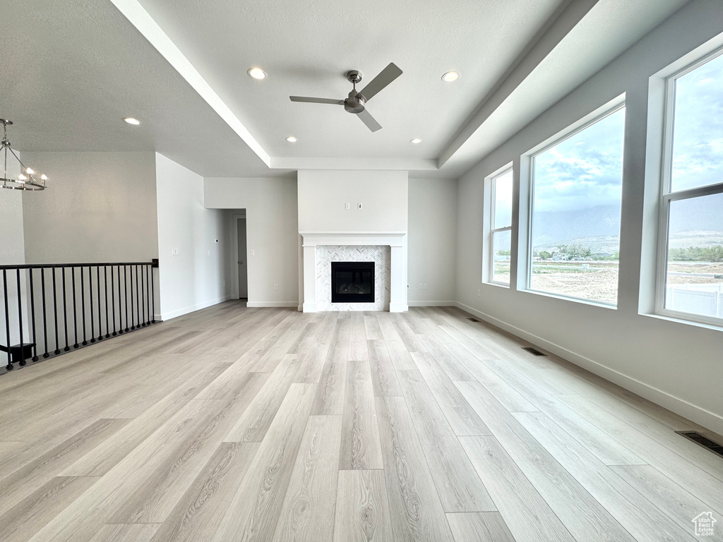 Unfurnished living room featuring plenty of natural light, a ceiling fan, light wood-type flooring, a tray ceiling, and recessed lighting