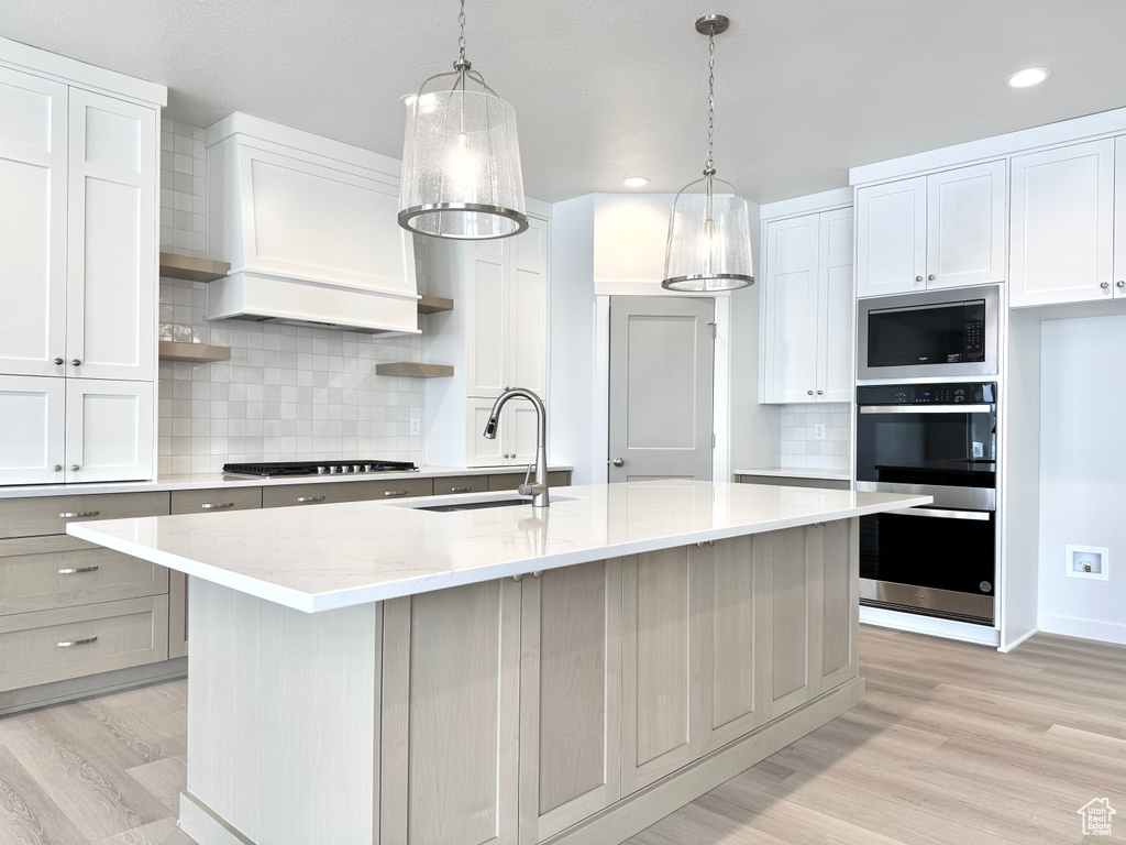 Kitchen with a sink, appliances with stainless steel finishes, open shelves, light wood-style floors, and tasteful backsplash