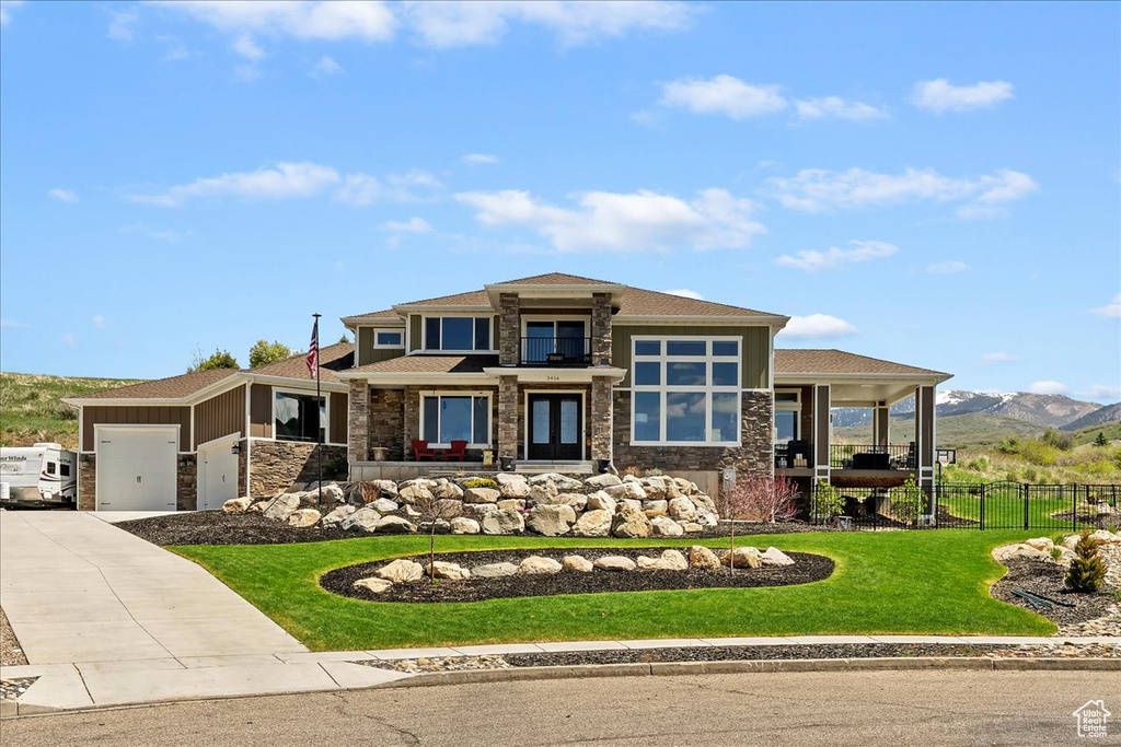 Prairie-style house featuring stone siding, an attached garage, driveway, a mountain view, and a porch