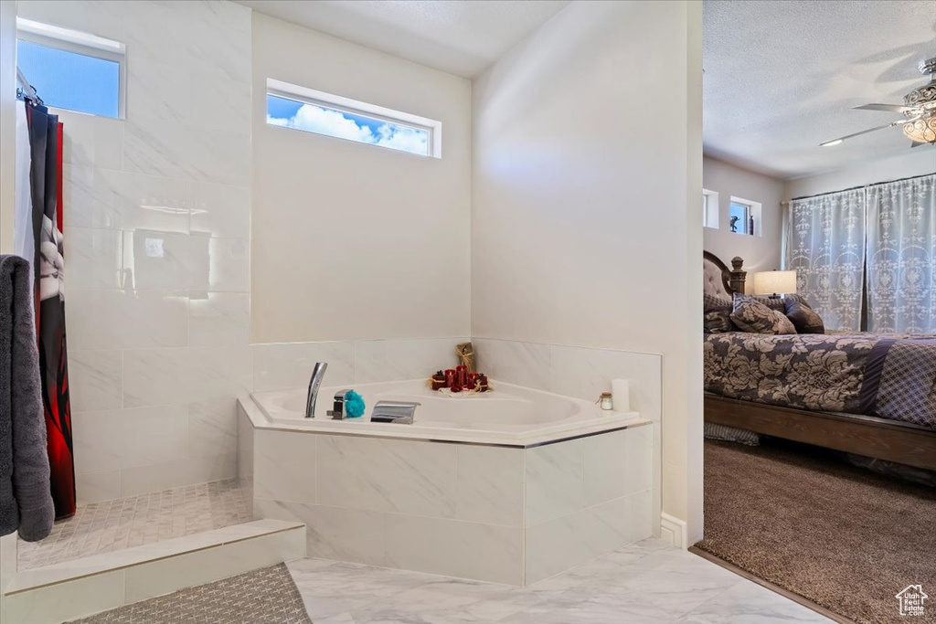 Bathroom with healthy amount of natural light, marble finish floors, a bath, and tiled shower