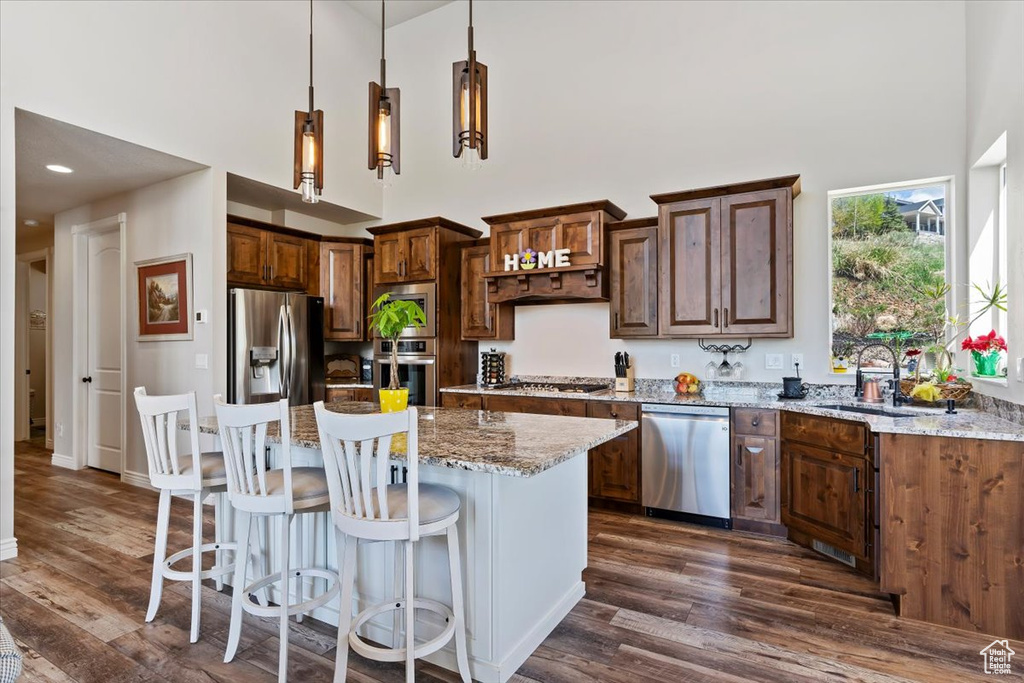 Kitchen featuring appliances with stainless steel finishes, a high ceiling, a sink, dark wood finished floors, and light stone counters