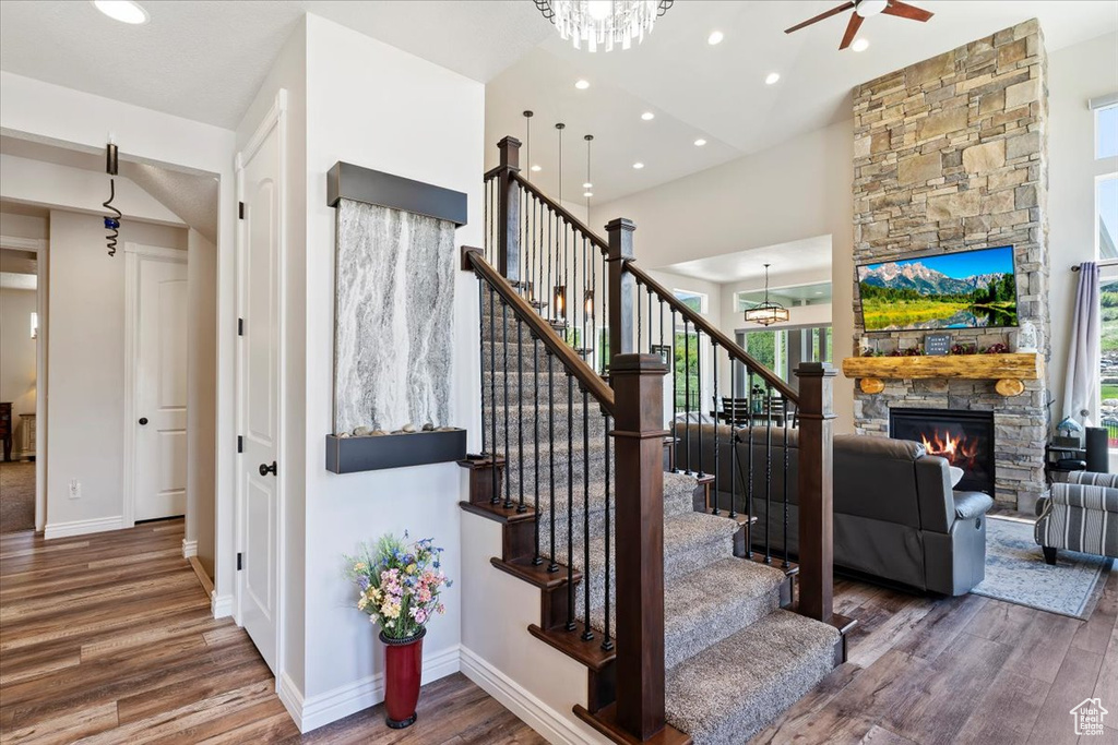 Stairs featuring wood finished floors, ceiling fan, a stone fireplace, baseboards, and recessed lighting