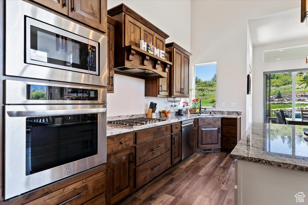 Kitchen featuring appliances with stainless steel finishes, light stone countertops, dark wood-type flooring, and dark brown cabinets