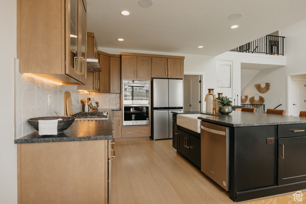 Kitchen with stainless steel appliances, a sink, under cabinet range hood, dark countertops, and tasteful backsplash