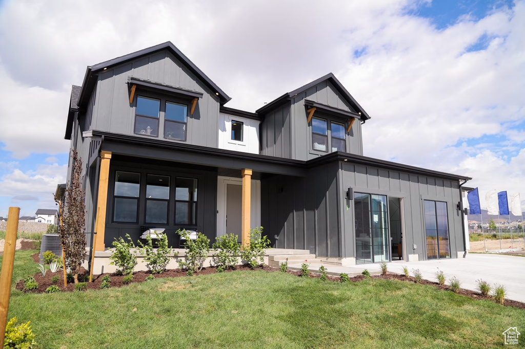 View of front facade with board and batten siding, a front yard, and cooling unit