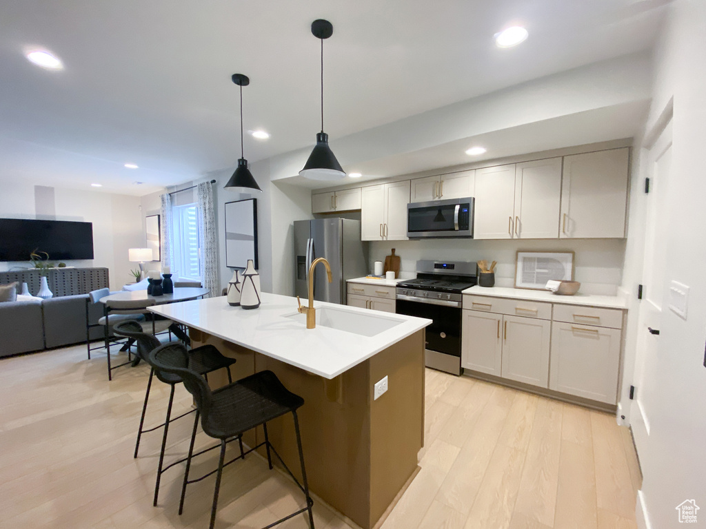 Kitchen featuring appliances with stainless steel finishes, a sink, light wood finished floors, recessed lighting, and a breakfast bar area