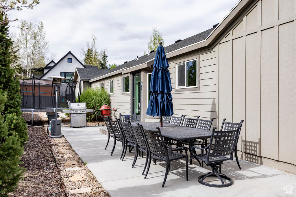 View of patio with a trampoline, outdoor dining area, and area for grilling