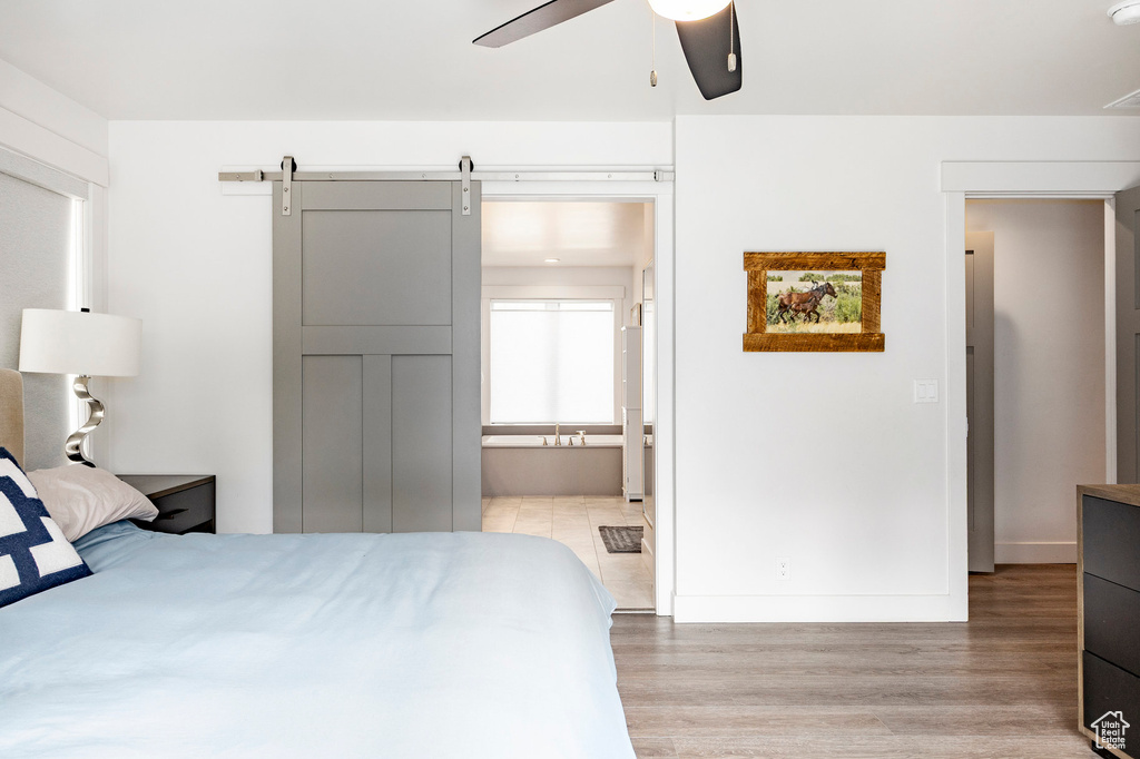 Bedroom featuring light wood finished floors, baseboards, ensuite bath, a ceiling fan, and a barn door
