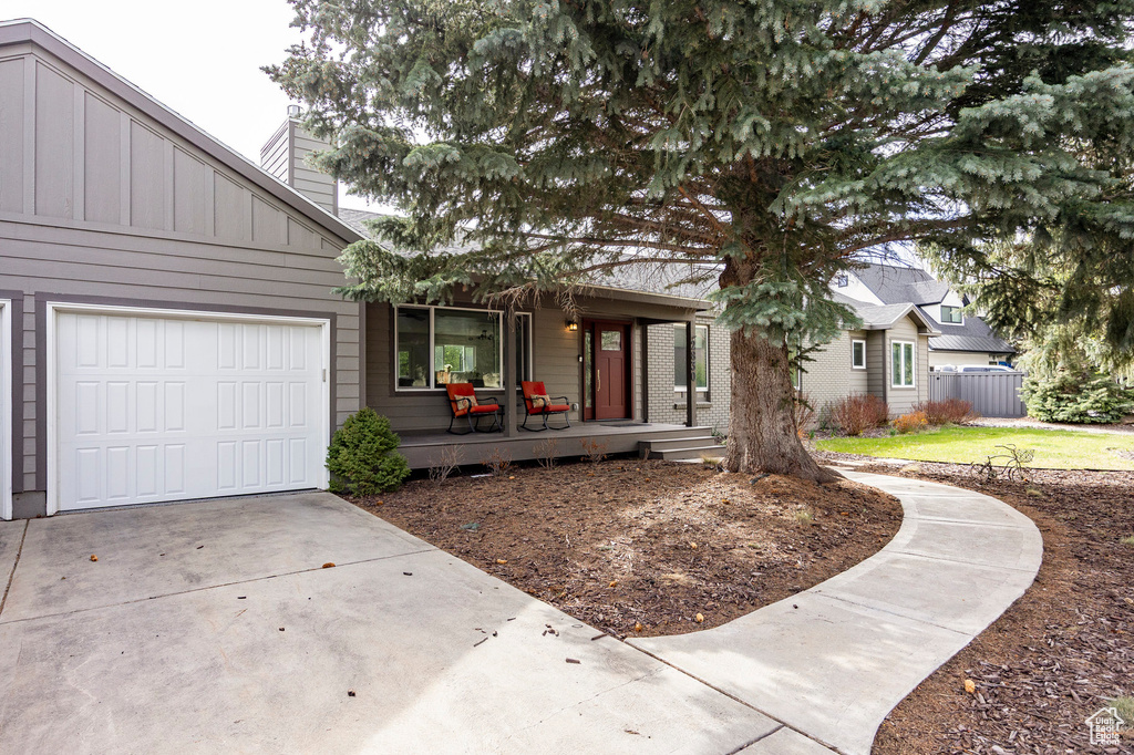 View of front of house with covered porch, a chimney, driveway, board and batten siding, and a garage