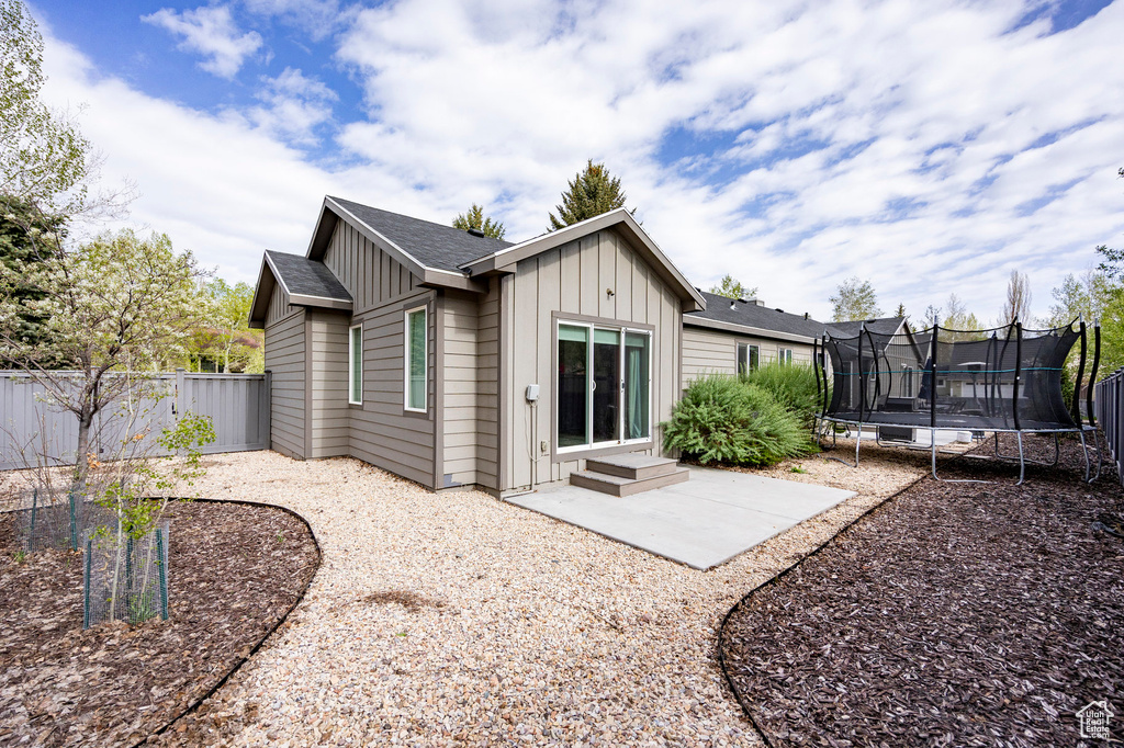 Back of property featuring a trampoline, board and batten siding, a fenced backyard, and a patio