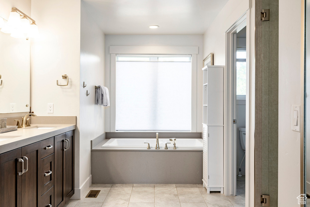 Bathroom featuring double vanity, a garden tub, tile patterned floors, and toilet