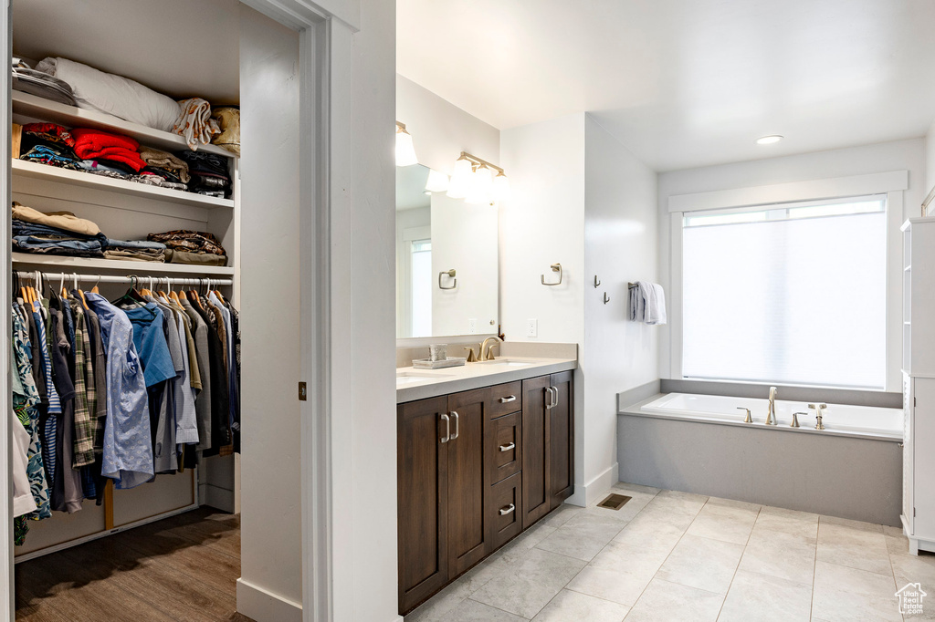 Full bath featuring vanity, a spacious closet, a garden tub, recessed lighting, and baseboards