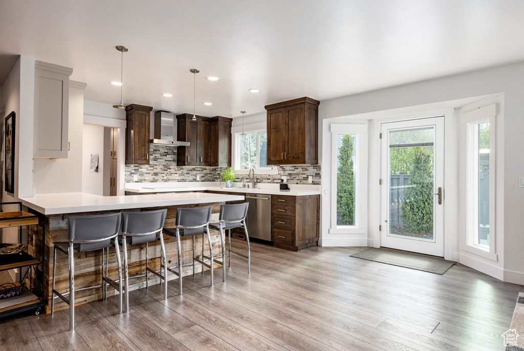Kitchen with dishwasher, wall chimney exhaust hood, dark brown cabinetry, a breakfast bar, and decorative backsplash