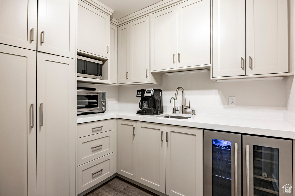 Kitchen featuring beverage cooler, a sink, light countertops, and stainless steel microwave