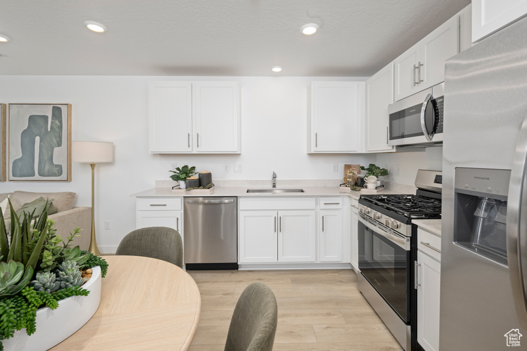 Kitchen featuring appliances with stainless steel finishes, a sink, light countertops, white cabinetry, and light wood-type flooring
