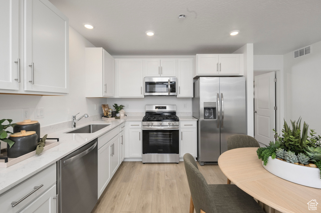 Kitchen with stainless steel appliances, a sink, light wood-style floors, white cabinets, and light stone counters
