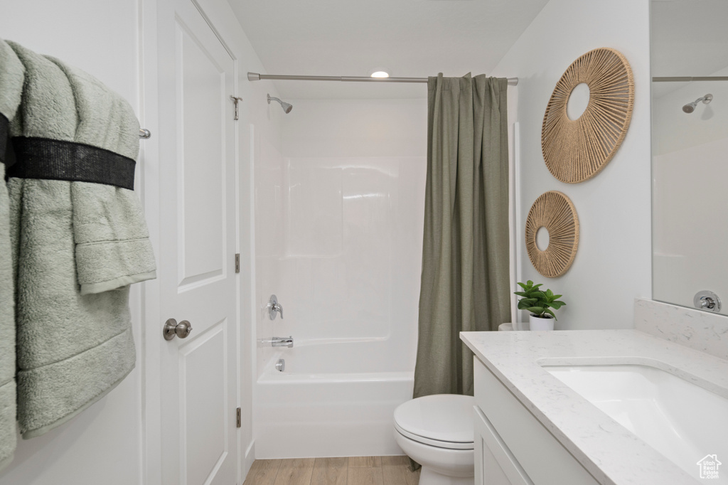 Full bath featuring shower / bath combo, toilet, vanity, and wood finished floors