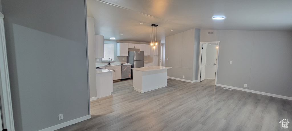 Kitchen featuring a center island, a sink, white cabinets, light countertops, and appliances with stainless steel finishes
