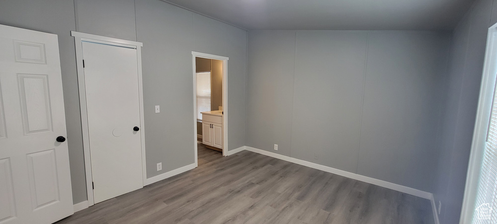 Unfurnished bedroom with baseboards, ensuite bathroom, and wood finished floors