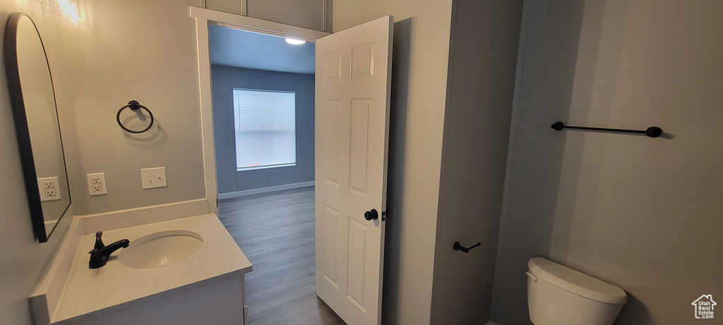 Half bath with toilet, baseboards, vanity, and wood finished floors