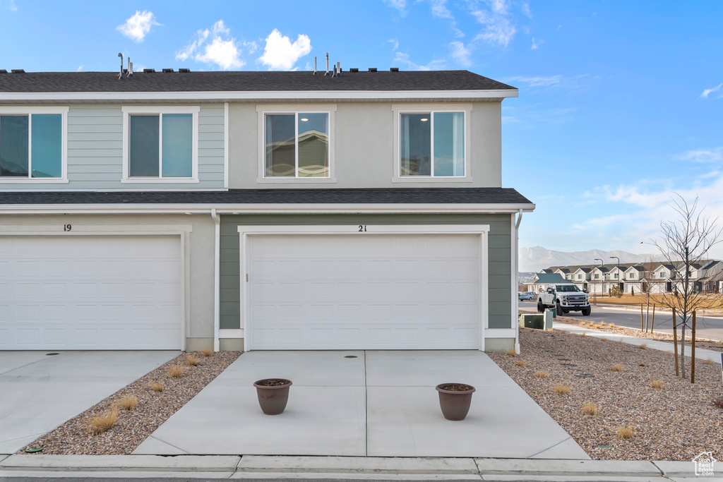 View of front of house featuring a garage, concrete driveway, and a shingled roof
