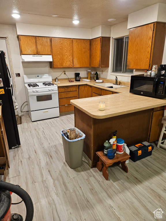 Kitchen featuring black appliances, a peninsula, brown cabinets, light wood-type flooring, and recessed lighting