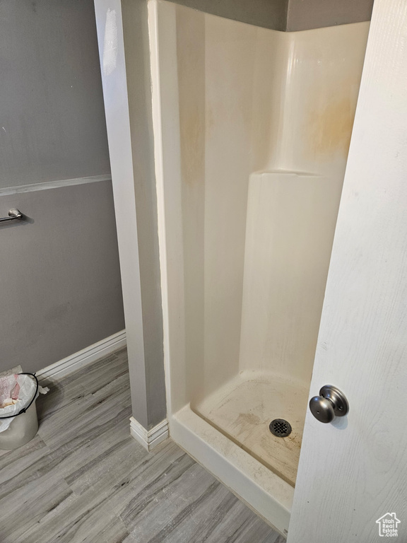 Bathroom with wood finished floors, a shower stall, and baseboards