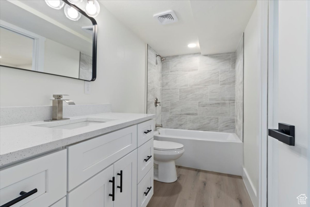 Bathroom with wood finished floors, toilet, vanity, shower / bathtub combination, and recessed lighting