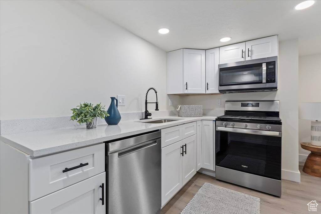 Kitchen with stainless steel appliances, a sink, white cabinets, light wood finished floors, and recessed lighting