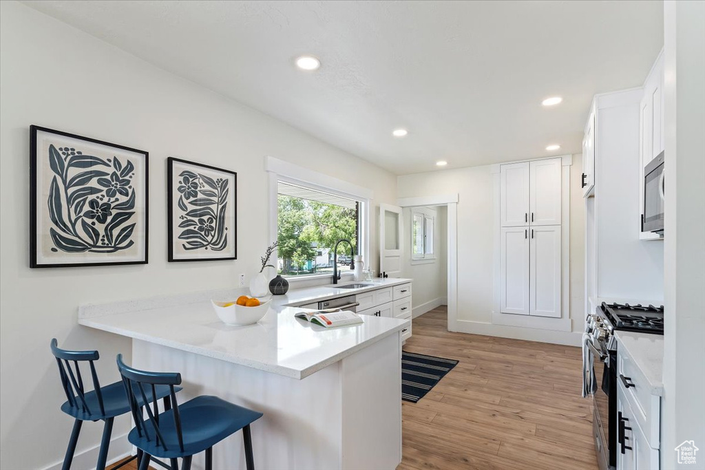 Kitchen with appliances with stainless steel finishes, a kitchen breakfast bar, a peninsula, a sink, and white cabinets