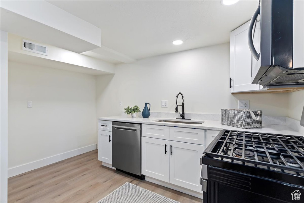 Kitchen featuring dishwasher, a sink, light wood-style flooring, white cabinetry, and recessed lighting