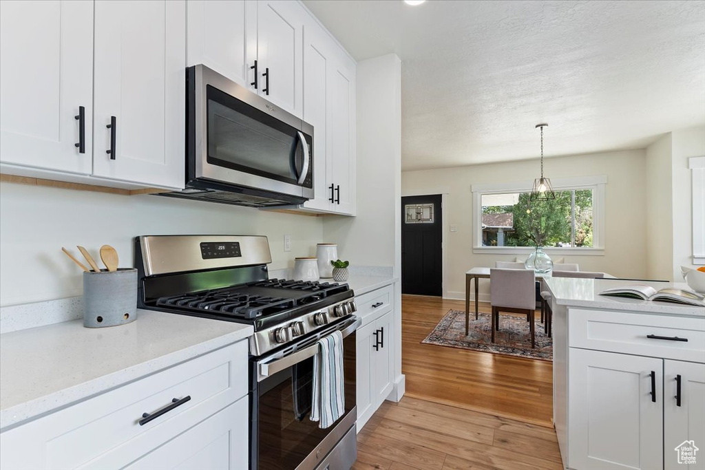 Kitchen with appliances with stainless steel finishes, light wood finished floors, white cabinets, and decorative light fixtures