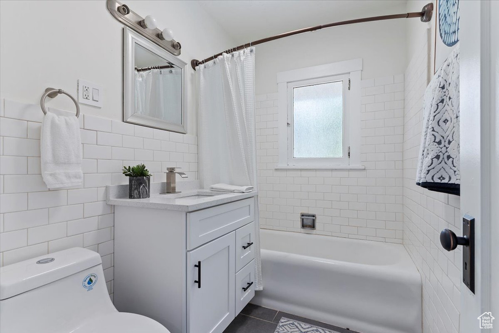 Bathroom with tile walls, tile patterned flooring, toilet, vanity, and shower / tub combo