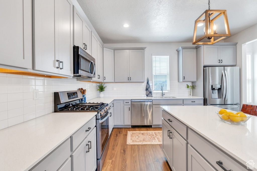 Kitchen with stainless steel appliances, a sink, light wood-type flooring, light countertops, and pendant lighting