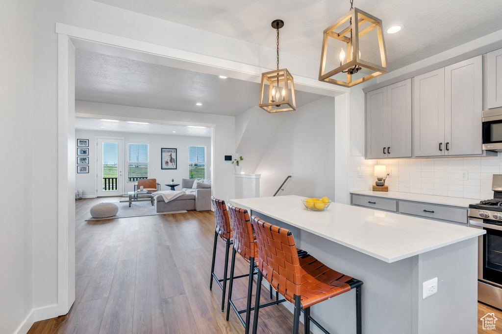 Kitchen with appliances with stainless steel finishes, a kitchen island, light countertops, backsplash, and wood finished floors