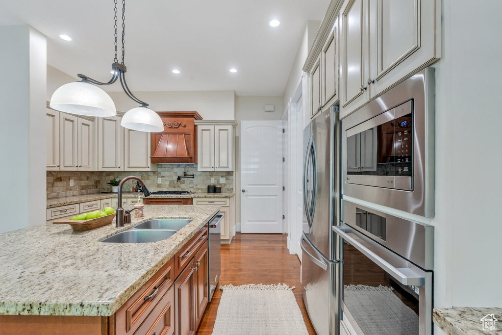 Kitchen featuring stainless steel appliances, a sink, backsplash, dark wood-type flooring, and light stone countertops