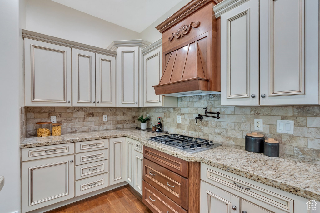 Kitchen featuring stainless steel gas stovetop, tasteful backsplash, light stone counters, wood finished floors, and custom exhaust hood