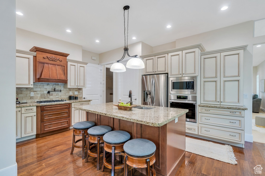 Kitchen featuring stainless steel appliances, decorative backsplash, dark wood finished floors, an island with sink, and light stone countertops