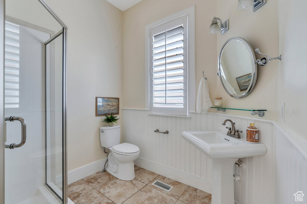 Full bath with wainscoting, a stall shower, toilet, and tile patterned flooring