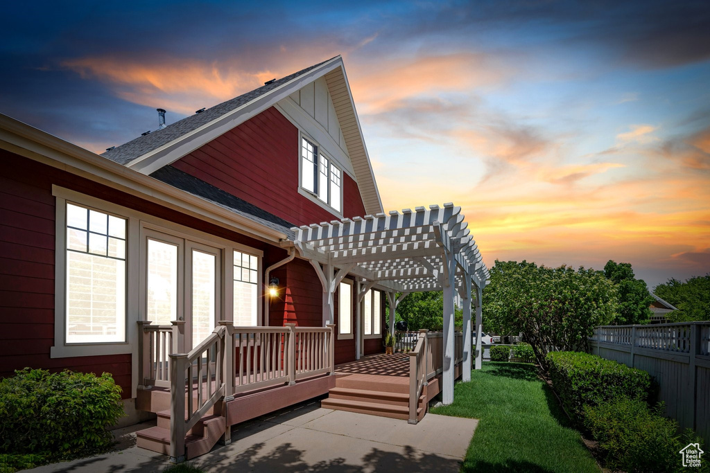Back of house at dusk with a pergola and fence