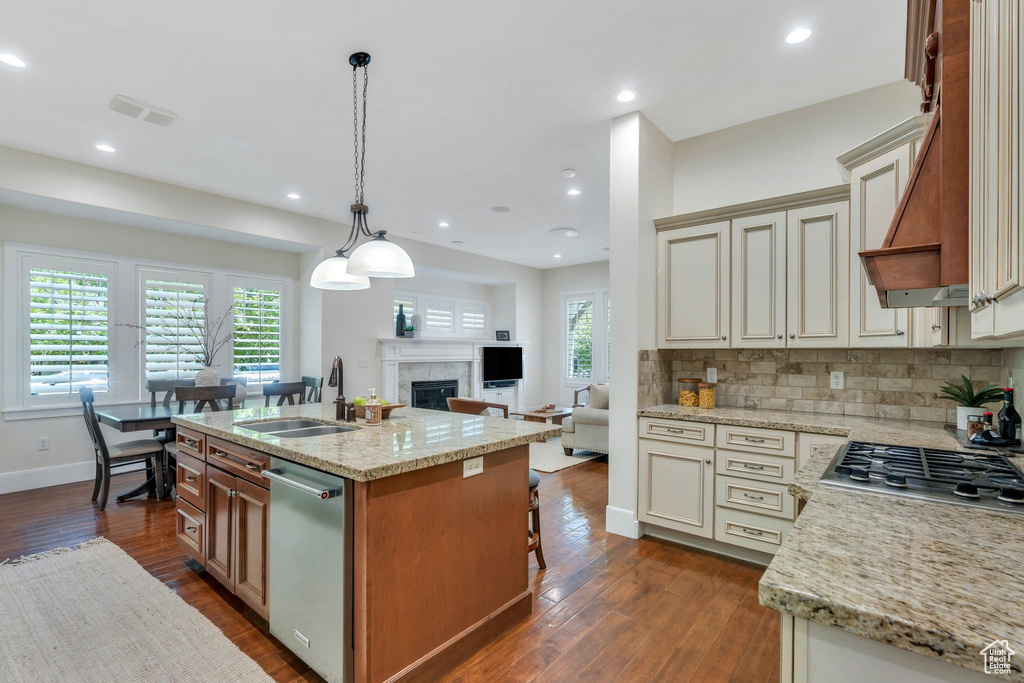 Kitchen featuring appliances with stainless steel finishes, a sink, open floor plan, cream cabinets, and dark wood-style floors