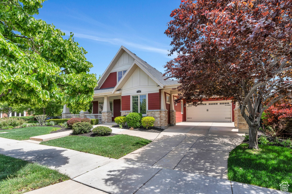 Craftsman inspired home featuring board and batten siding, driveway, stone siding, a porch, and an attached garage