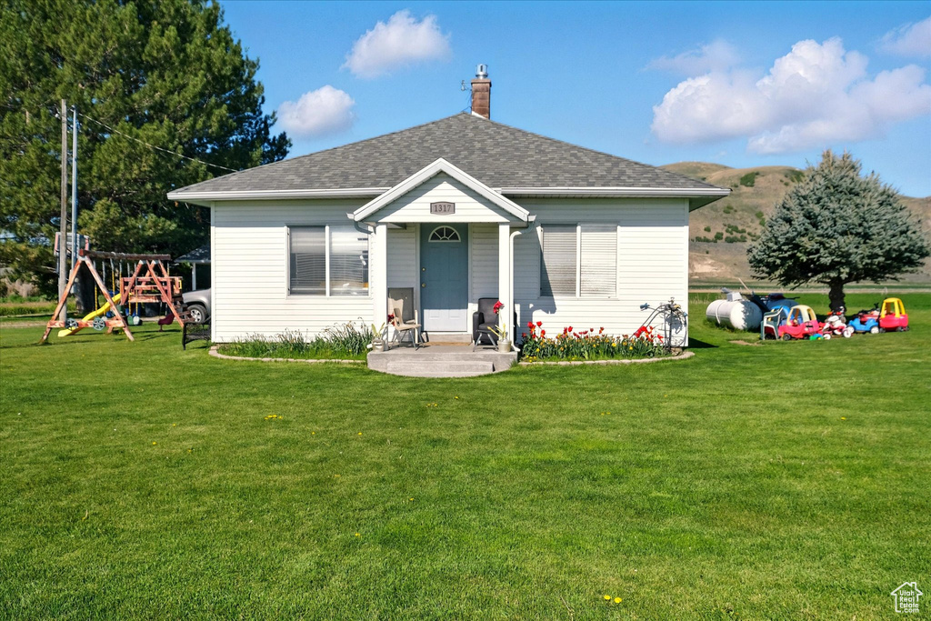 View of front of property with a playground, a front yard, a chimney, and a shingled roof